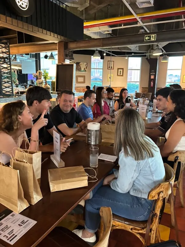 Alunos conversando ao redor da mesa comprida do restaurante, com as sacolas de brinde sobre a mesa