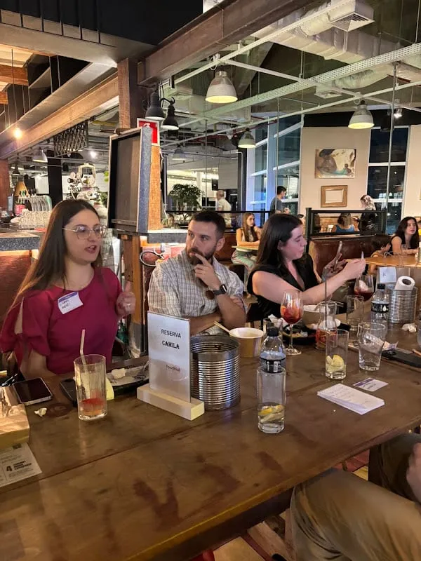 Alunos conversando à mesa, ao lado da placa de reserva no nome da Camila