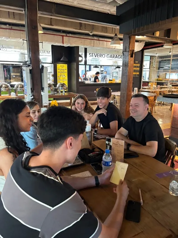Alunos rindo à mesa enquanto olham o cardápio, com o salão do restaurante ao fundo